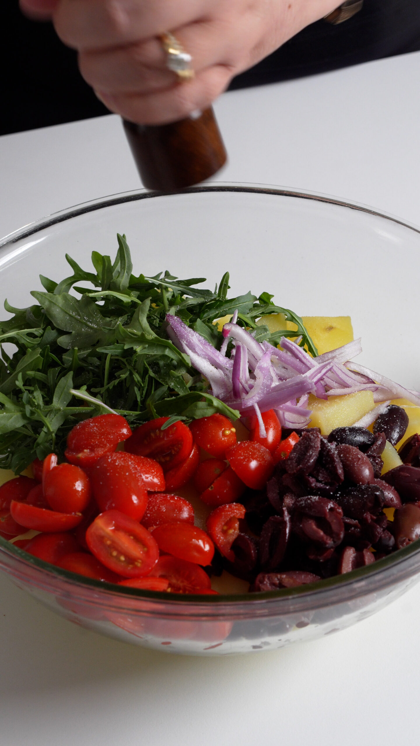 Cubed yukon gold potatoes in a bowl topped with olives, tomatoes, arugula and sliced red onions