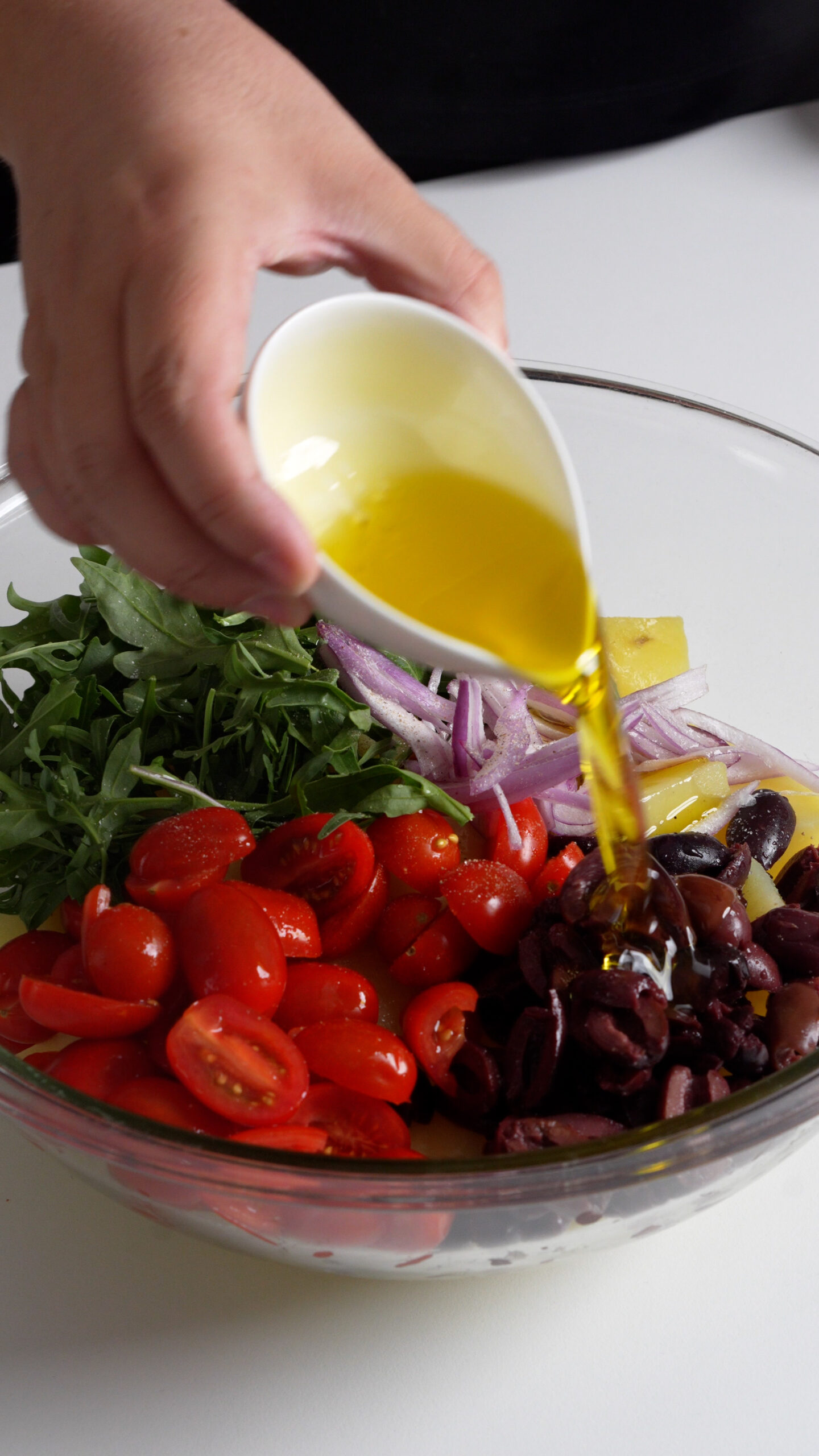 Olive oil being poured onto Italian potato salad with arugula